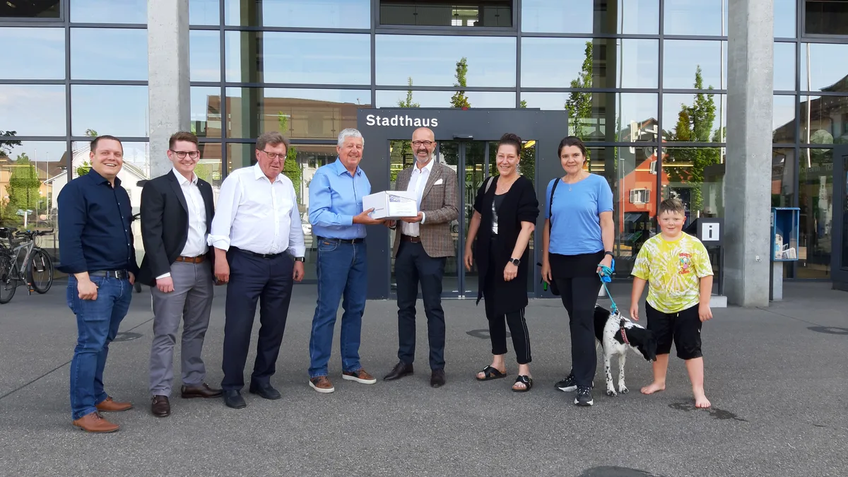 Eine Personengruppe steht vor einem Stadthaus mit Glasfassade.